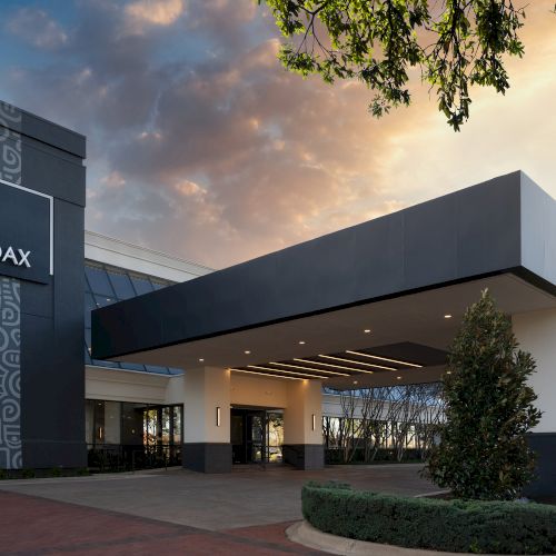 A modern house with a low, sloped roof, dark exterior, front porch, and lush landscaping under a cloudy sky.