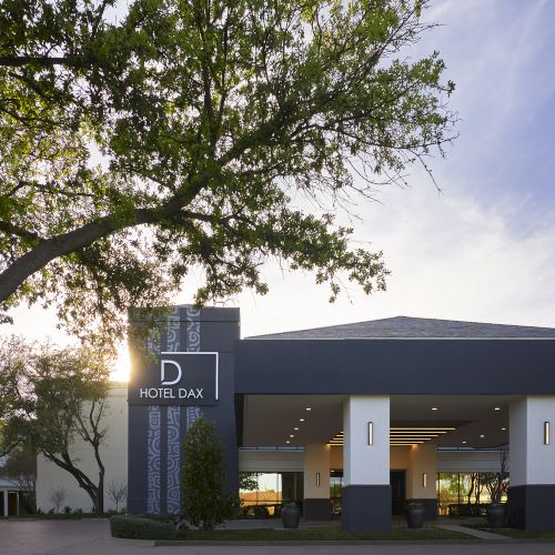 A small gray building with a flat roof beside a tree, set against a partly cloudy sky.