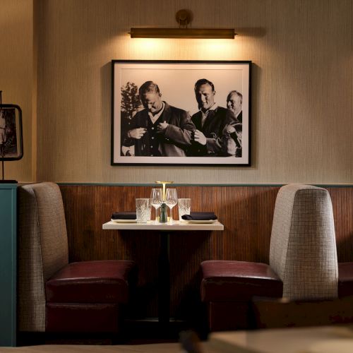 A cozy restaurant with booths, framed black-and-white photos, soft lighting, and a small bookshelf by the counter, warmly lit for dining.