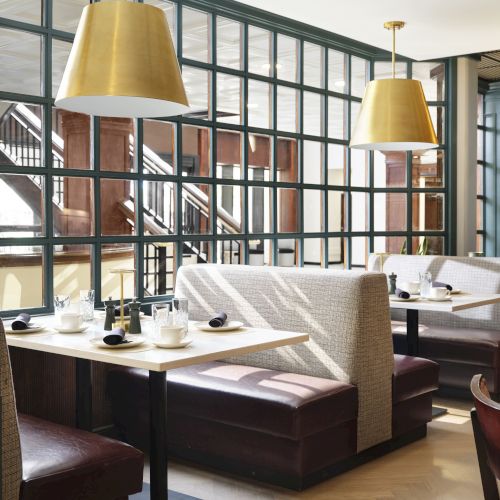 A stylish cafe with booth seating, wooden tables, large gold pendant lights, and a glass-paneled partition creating cozy dining nooks.