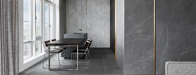 A modern, minimalist dining area with a sleek table, chairs, and large windows for natural light, featuring gray tones and clean lines.
