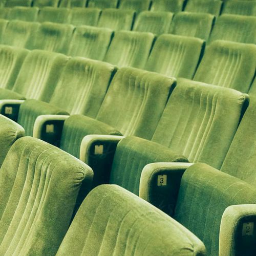 A row of empty green theater or stadium seats, evenly spaced and slightly worn, creating a repeating pattern and a quiet, overlooked space.
