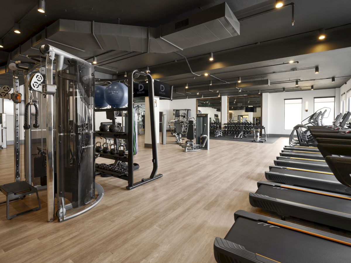 A modern gym with cardio machines on the right, weight machines and racks on the left, and open space in the center, bright and well lit.