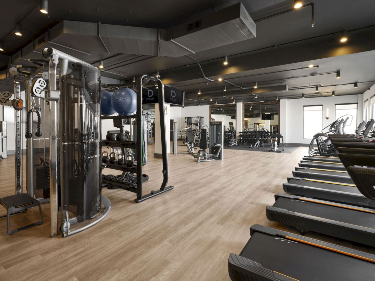 A modern gym with cardio machines, free weights, resistance machines, and a spacious wooden floor training area, bright and open.