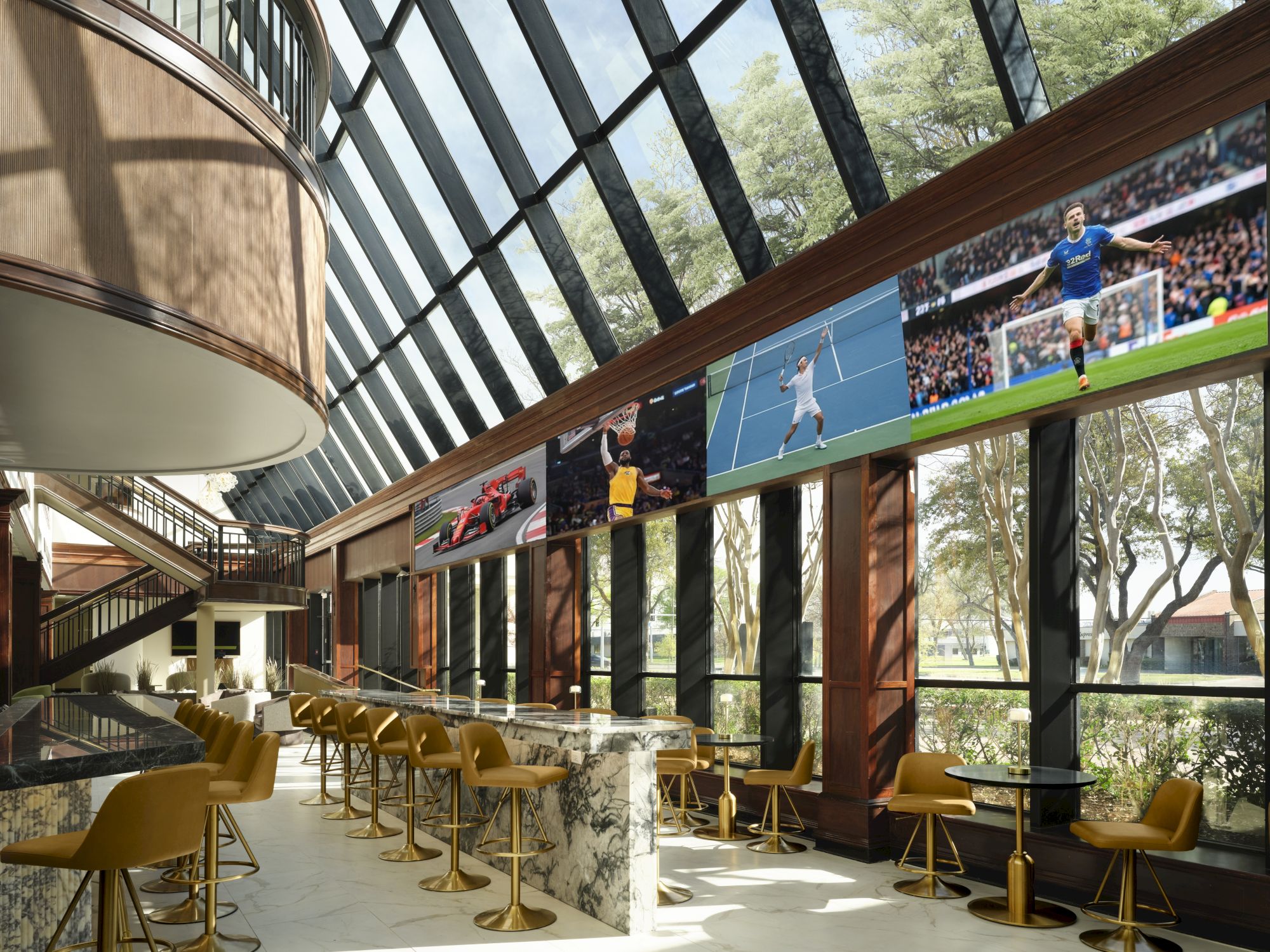 A modern, sunlit indoor cafe with yellow chairs, long counter, and large glass walls offering outdoor views, creating a spacious, airy vibe.