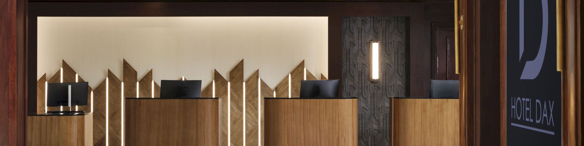 A hotel lobby with a marble floor, wooden reception desks, geometric gold accents, and a large &ldquo;D&rdquo; hotel sign at right.
