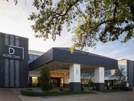 A modern hotel building named D Hotel Dax with a covered entrance, trees, and a clear sky in the background.