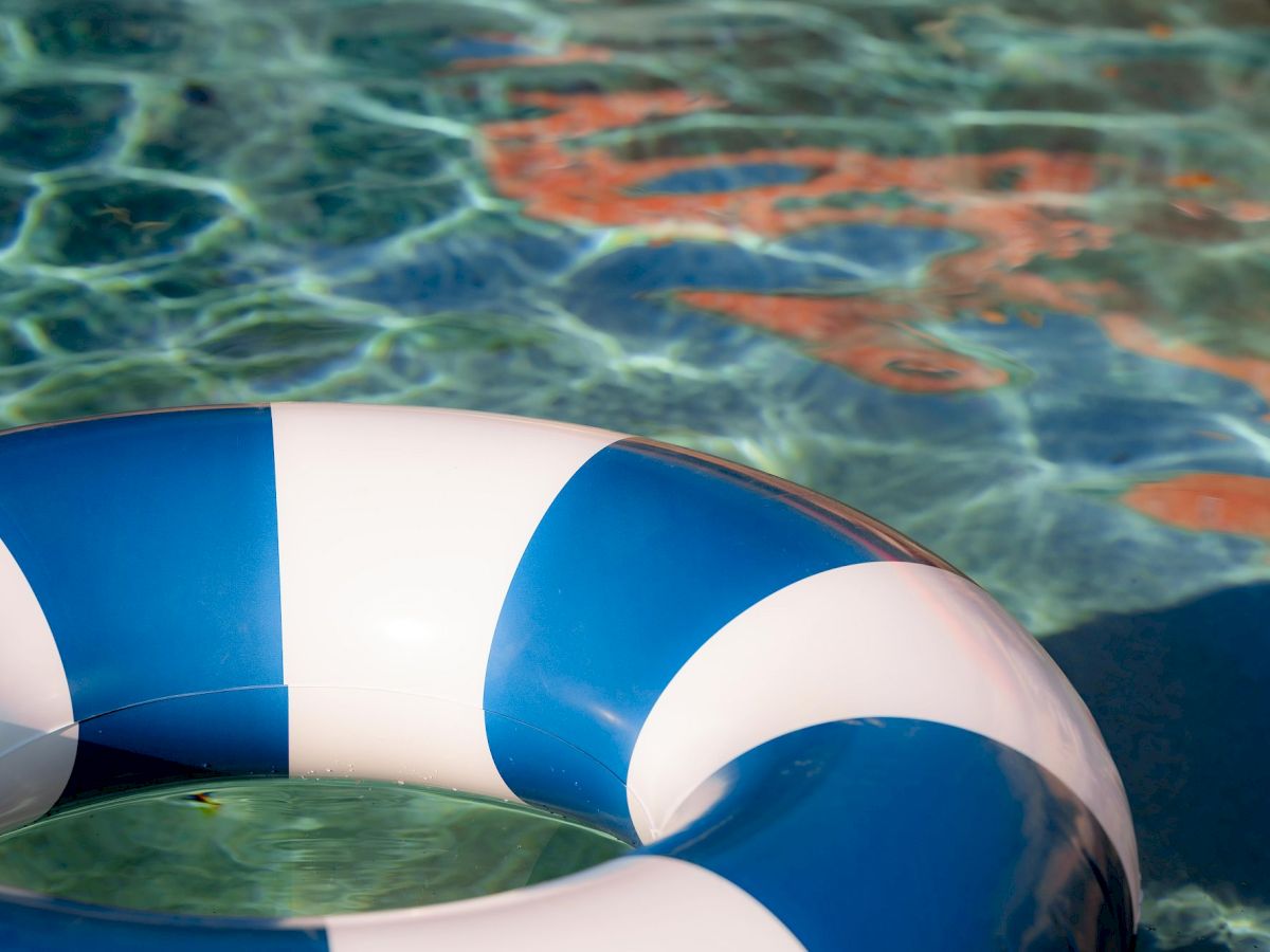 A blue-and-white striped lifebuoy floats on clear water as the pool&rsquo;s rippling reflections shimmer nearby.
